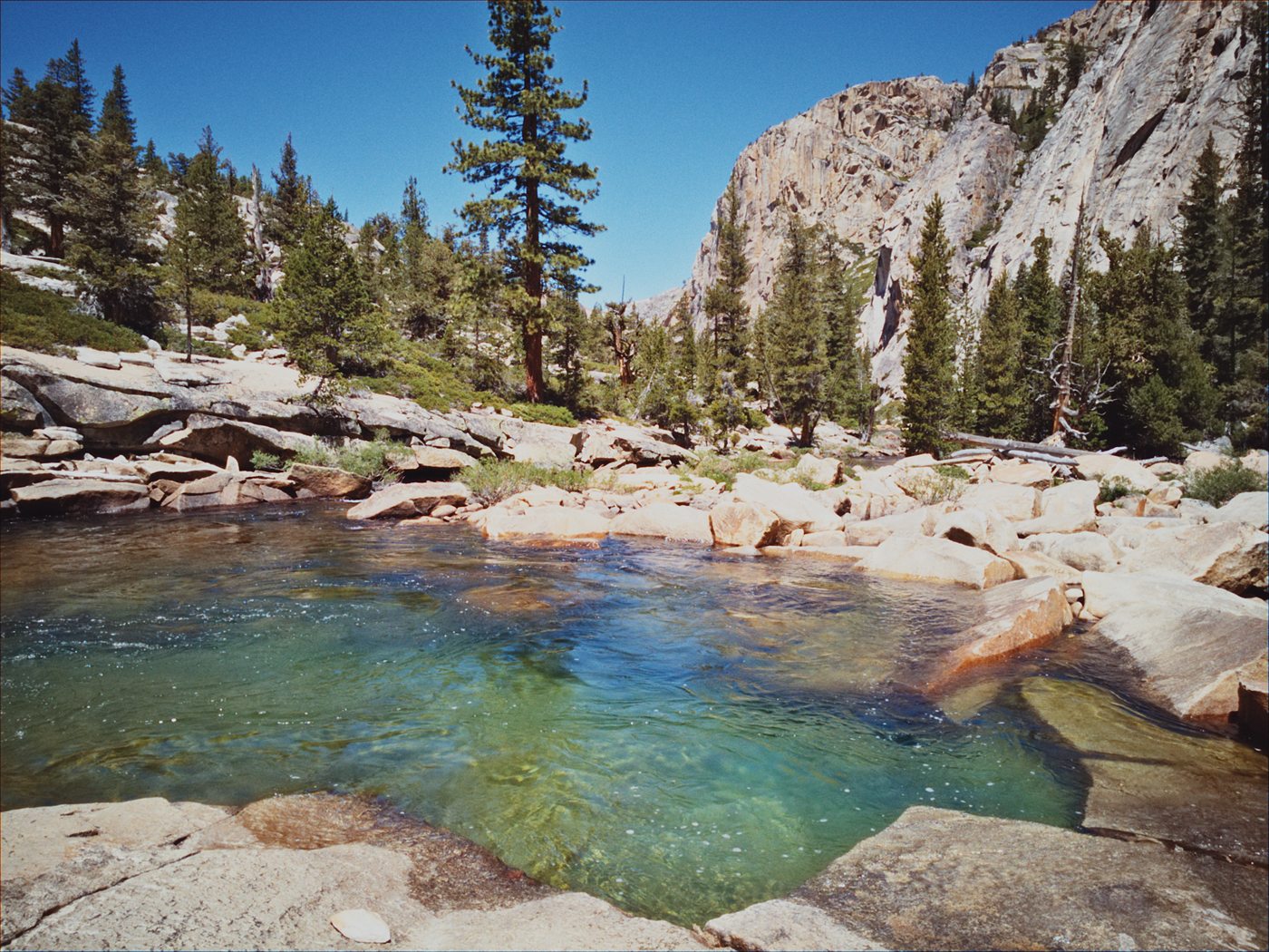Developed film photo of an alpine river pool below granite cliffs